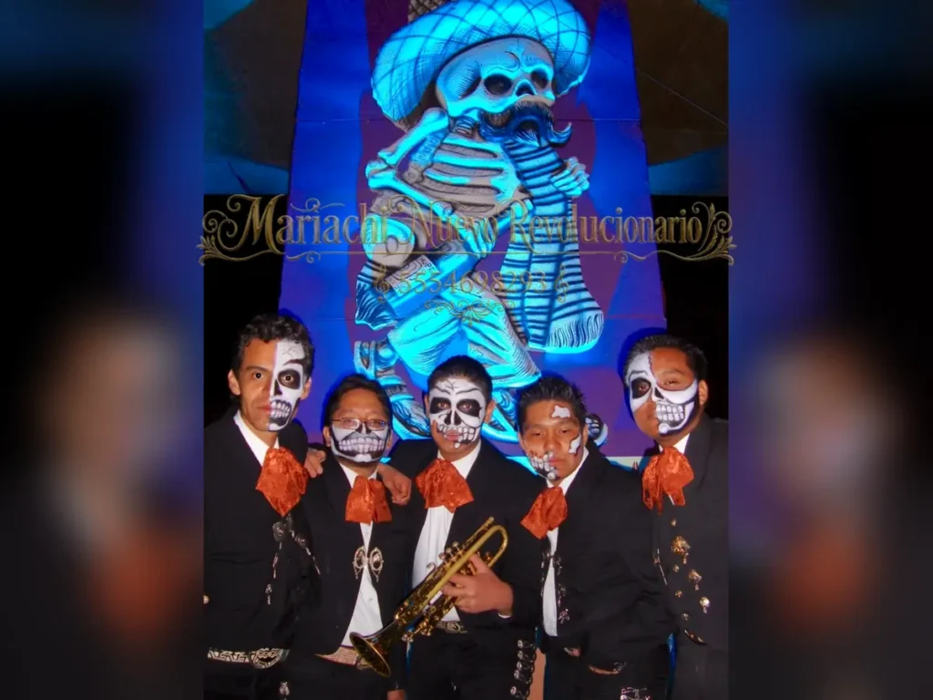 Grupo de cinco mariachis con maquillaje de calavera frente a una figura tradicional de Día de Muertos
